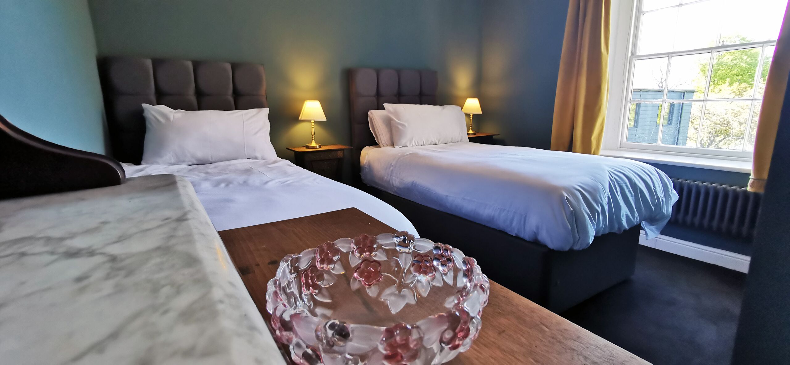 A hotel room with two beds, a marble bedside table, and a decorative glass bowl.