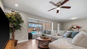 A spacious living room with a large sofa, a coffee table, and a ceiling fan. There is a potted plant and a view of a swimming pool outside. - The Shiny Diamond in Sarasota. 10 minutes to SIESTA BEACH (Sarasota)