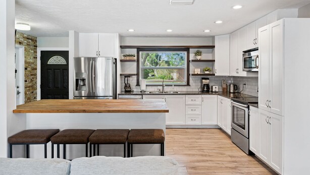 A modern kitchen with white cabinets, stainless steel appliances, and a wooden island with bar stools. - The Shiny Diamond in Sarasota. 10 minutes to SIESTA BEACH (Sarasota)