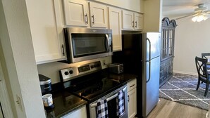 A compact kitchen with white cabinets, a microwave, stove, and refrigerator. - The Alex Furnished Rentals (Oshkosh)