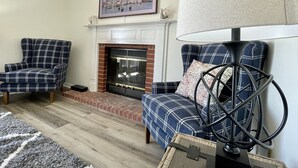 A living room with a fireplace, two plaid armchairs, a rug, and a framed picture on the wall. - The Alex Furnished Rentals (Oshkosh)