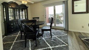 A dining area with a table and chairs, a ceiling fan, a large window with a view of the outdoors, and a dark wooden cabinet. - The Alex Furnished Rentals (Oshkosh)