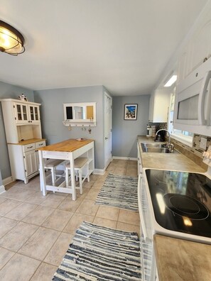 Una cocina con mesa de madera, armarios blancos, estufa y piso de baldosas.