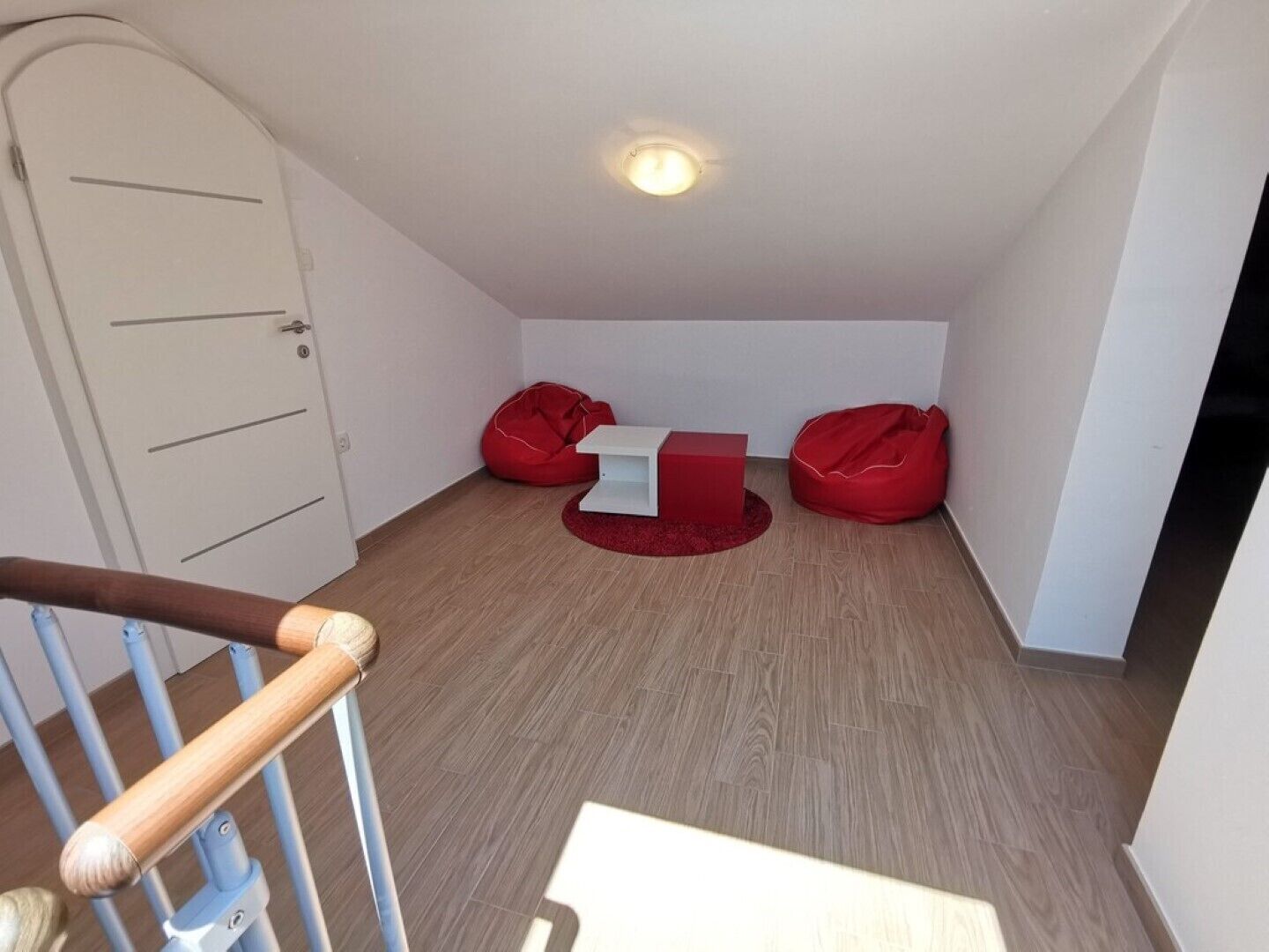 A small, well-lit attic room with a wooden staircase, a white door, and two red bean bags.