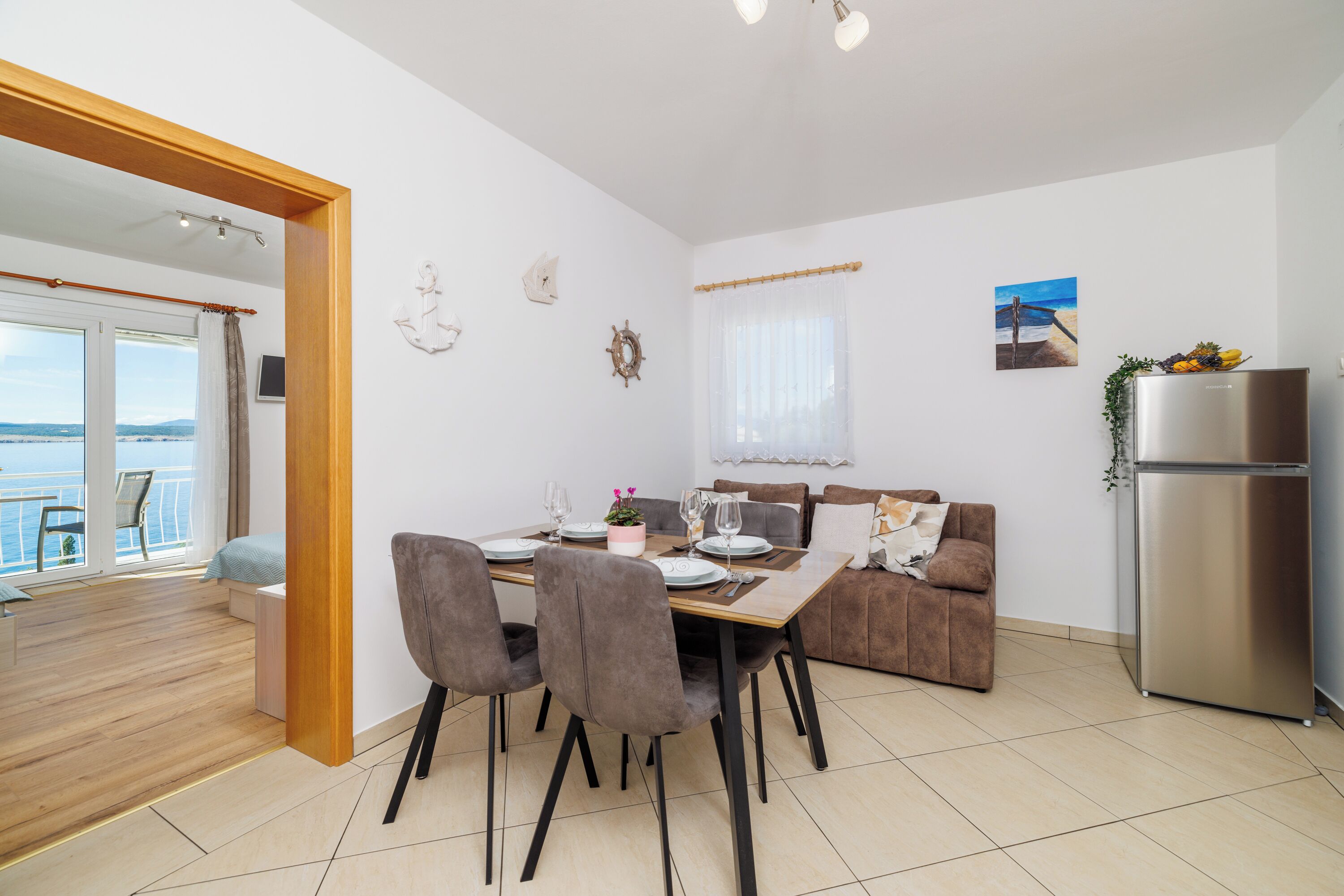 A modern kitchen with a dining area, a sofa, and a view of the sea.