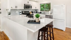 Une cuisine moderne avec des meubles blancs, un grand îlot central et un réfrigérateur en acier inoxydable.