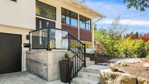 Une maison moderne à deux étages, dotée d’un escalier en béton, d’une rambarde noire et d’une porte de garage.