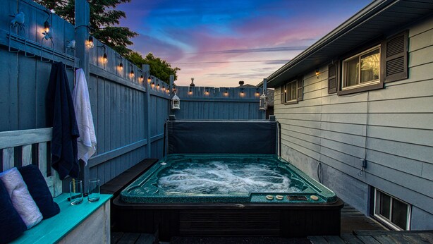 A hot tub in a backyard with a wooden fence and string lights. - Hot Tub Haven w/ King Bed + More (Greater Sudbury)