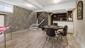 A spacious room with a ping pong table, a dartboard, and a bar area with shelves of bottles. - Hot Tub Haven w/ King Bed + More (Greater Sudbury)
