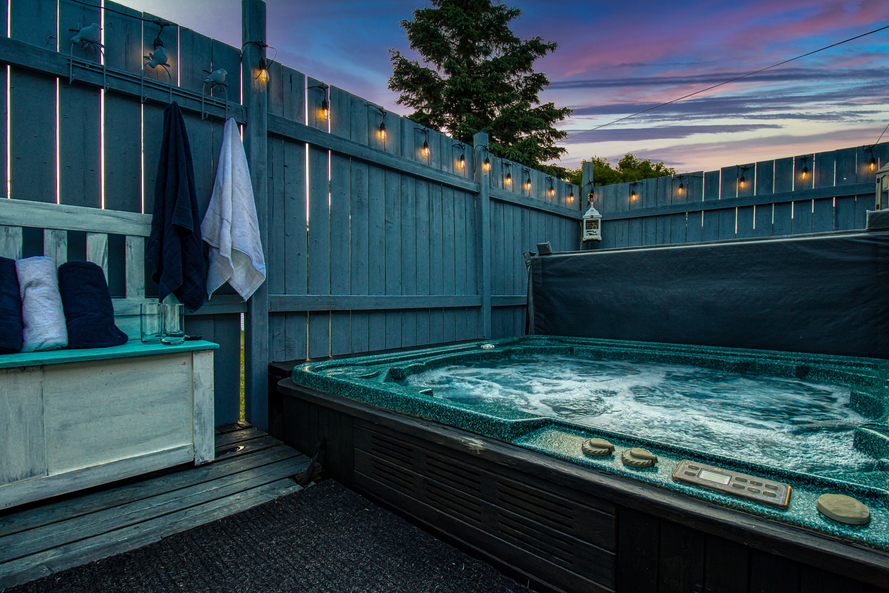 A hot tub with a wooden deck, surrounded by a wooden fence with string lights.