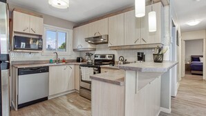A modern kitchen with light wood cabinets, stainless steel appliances, and a central island. - Hot Tub Haven w/ King Bed + More (Greater Sudbury)