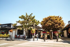 A public square with a restaurant named "HEEL'S GINGER BEER," outdoor seating, and trees.