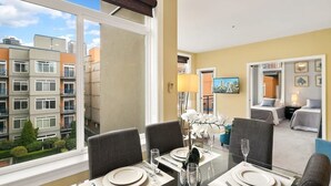 A dining area with a table set for four, a vase with white flowers, and a cityscape view through large windows. - Amazing Courtyard View DT Parking tub pool 99 WS (Seattle)