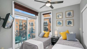 A hotel room with two beds, a ceiling fan, a TV mounted on the wall, and a balcony with a view of other buildings. - Amazing Courtyard View DT Parking tub pool 99 WS (Seattle)
