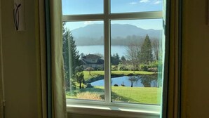 A window with a view of a lake, a house, and mountains in the distance. - Elegant 4400sf Villa w/ Lk. & Mt. view | Sammamish (Sammamish)
