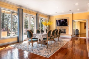 A dining area with a table set for six, surrounded by chairs, large windows, and a fireplace.