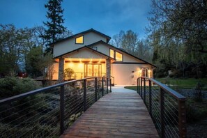 Una casa moderna con una terraza de madera que conduce a la entrada, rodeada de árboles.