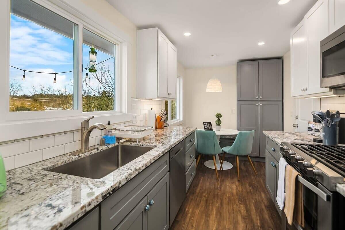 A modern kitchen with granite countertops, a stainless steel sink, and a built-in stove. There is a dining area with a table and two chairs.