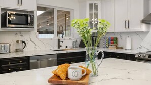 Ett modernt kök med vita skåp, en bänkskiva i marmor, en kaffekopp, croissanter och en vas med blommor.