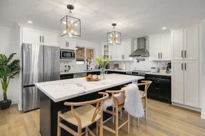 Una cocina moderna con armarios blancos, electrodomésticos de acero inoxidable, una isla de mármol y sillas de madera.