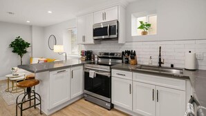 A modern kitchen with white cabinets, stainless steel appliances, and a central island with stools. - Brand New Designer's Modern, 1BR Home 1min to I-5 (Lynnwood)