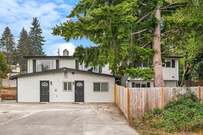 A single-story house with a garage, a fenced yard, and a large tree in front.