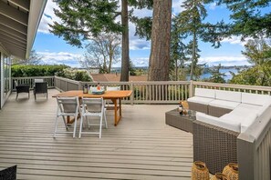 A wooden deck with a table and chairs, a sofa, and wicker baskets. - Family Retreat w Lake & Mt & City View, Gym, MI (Mercer Island)