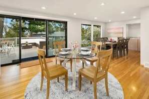 A dining area with a glass table surrounded by wooden chairs, a kitchen area with wooden cabinets, and a view of a deck with outdoor furniture. - Family Retreat w Lake & Mt & City View, Gym, MI (Mercer Island)