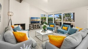 A modern living room with grey sofas, a coffee table, and a TV. There is a fireplace, a large window with a view, and a balcony. - Family Retreat w Lake & Mt & City View, Gym, MI (Mercer Island)