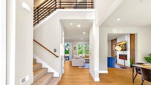 Ein geräumiger Innenraum mit einer Treppe, die zu einer zweiten Etage führt, einem Wohnbereich mit Kamin und einem Essbereich mit Tisch und Stühlen.