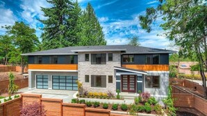 Ein modernes, zweistöckiges Haus mit Natursteinfassade, großen Fenstern und einer Garage.