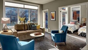 Un salon moderne comprenant un canapé, deux fauteuils, une table basse et une grande fenêtre donnant sur la ville.