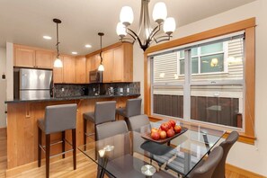 Eine moderne Küche mit Holzausbau, einem Edelstahlkühlschrank, einem Glastisch mit Stühlen und einer Kronleuchter.