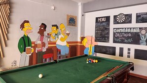 A pool table with a chalkboard menu listing food and drinks, a dartboard, and a sign for a hostel. -  Solsticio Copacabana (Copacabana)