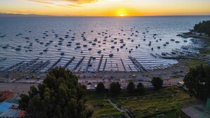 A marina with numerous boats docked, a sunset in the background, and a view of the surrounding landscape including trees and buildings. -  Solsticio Copacabana (Copacabana)