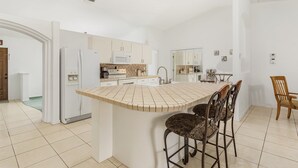 Een moderne keuken met een centraal eiland, witte kasten en een eethoek met een houten stoel.