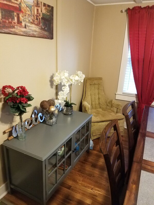 A dining area with a wooden table and chairs, a grey console table with decorative items, a beige armchair, and a painting on the wall.