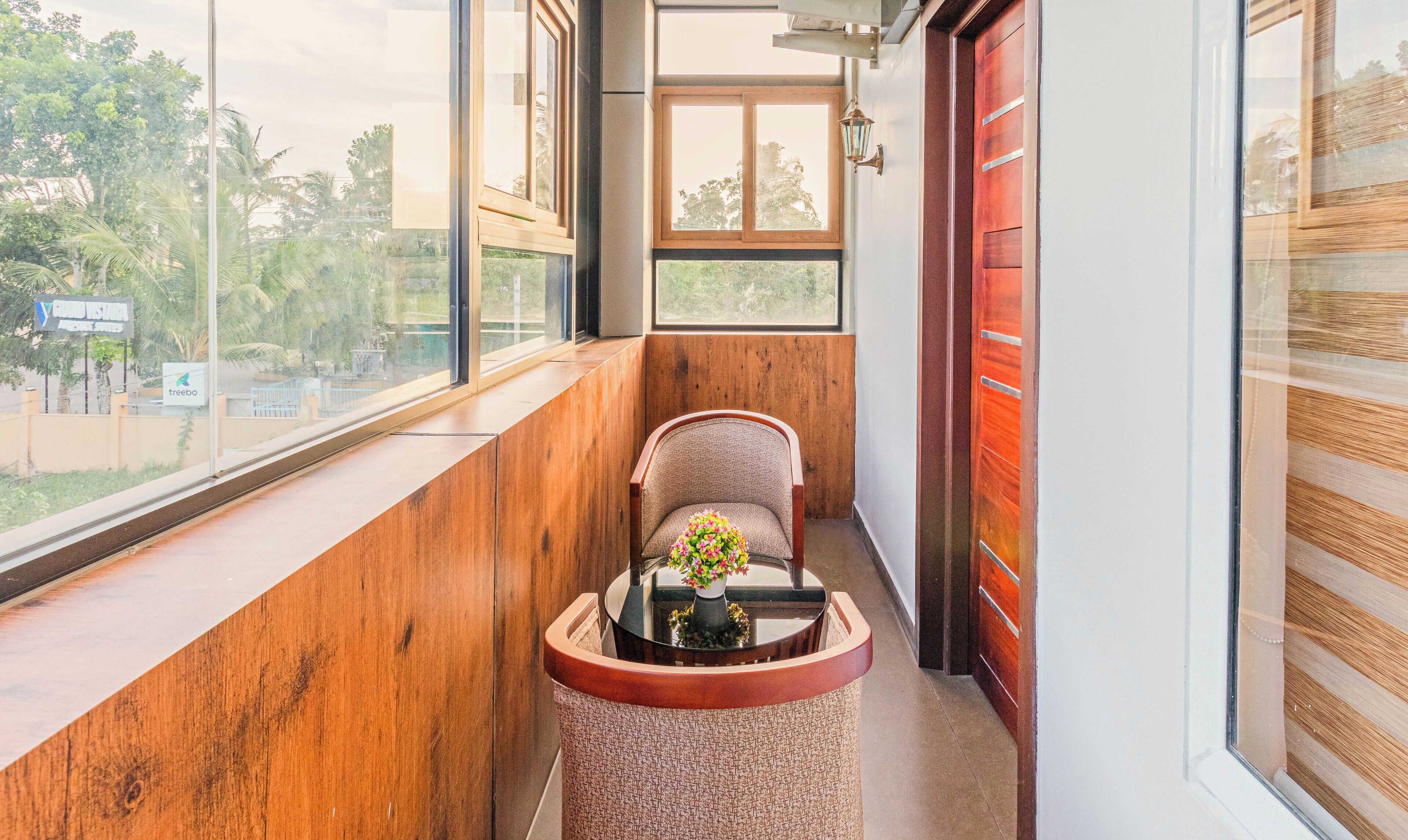 A narrow balcony with a wooden floor, a chair, and a small table with a vase of flowers.
