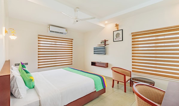 Habitación de hotel con cama, escritorio y silla. Se observa un equipo de aire acondicionado en la pared y un ventilador de techo.