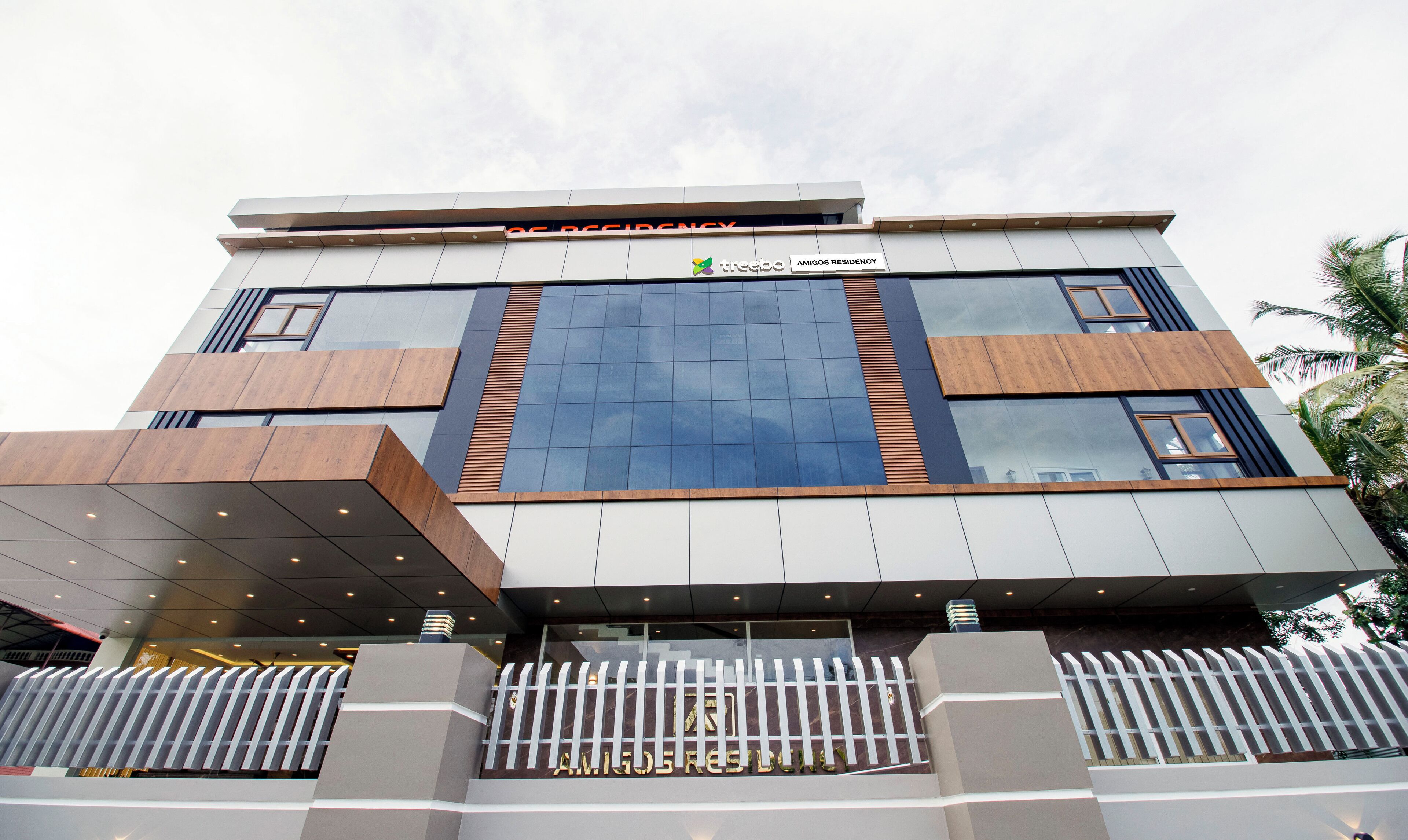 A modern building with a prominent 'Amigos Residency' sign, large glass windows, and a geometric facade design.