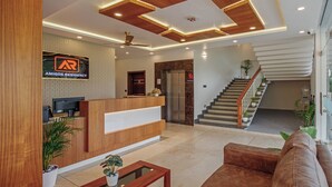 A modern reception area with a wooden reception desk, a digital screen, a staircase, and potted plants. - Treebo Amigos Residency Cochin Airport Hotel (Aluva)