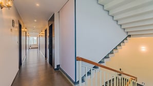 A modern hotel hallway with a wooden floor, a staircase with white railings, and wall-mounted lighting. - Treebo Amigos Residency Cochin Airport Hotel (Aluva)