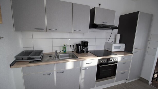 Eine moderne Küche mit grauen Schränken, einer Holz Arbeitsplatte, einem eingebauten Backofen und einer Mikrowelle.