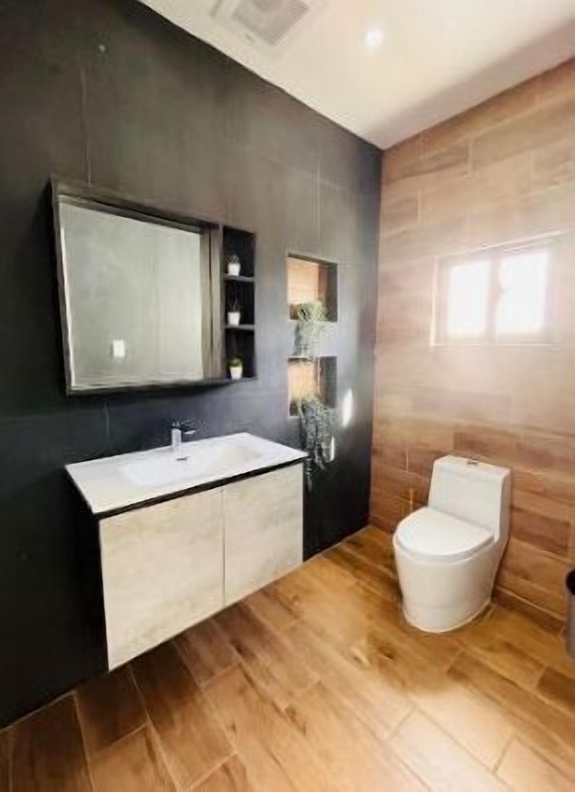 Ein modernes Badezimmer mit dunkler Wand, einem großen Spiegel, einem weißen Waschbecken und einer Toilette.