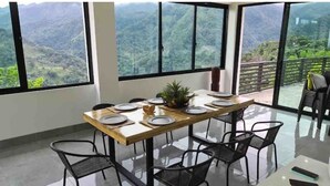 Comedor con mesa preparada para cuatro personas, ventanas amplias que ofrecen vistas a un paisaje montañoso.