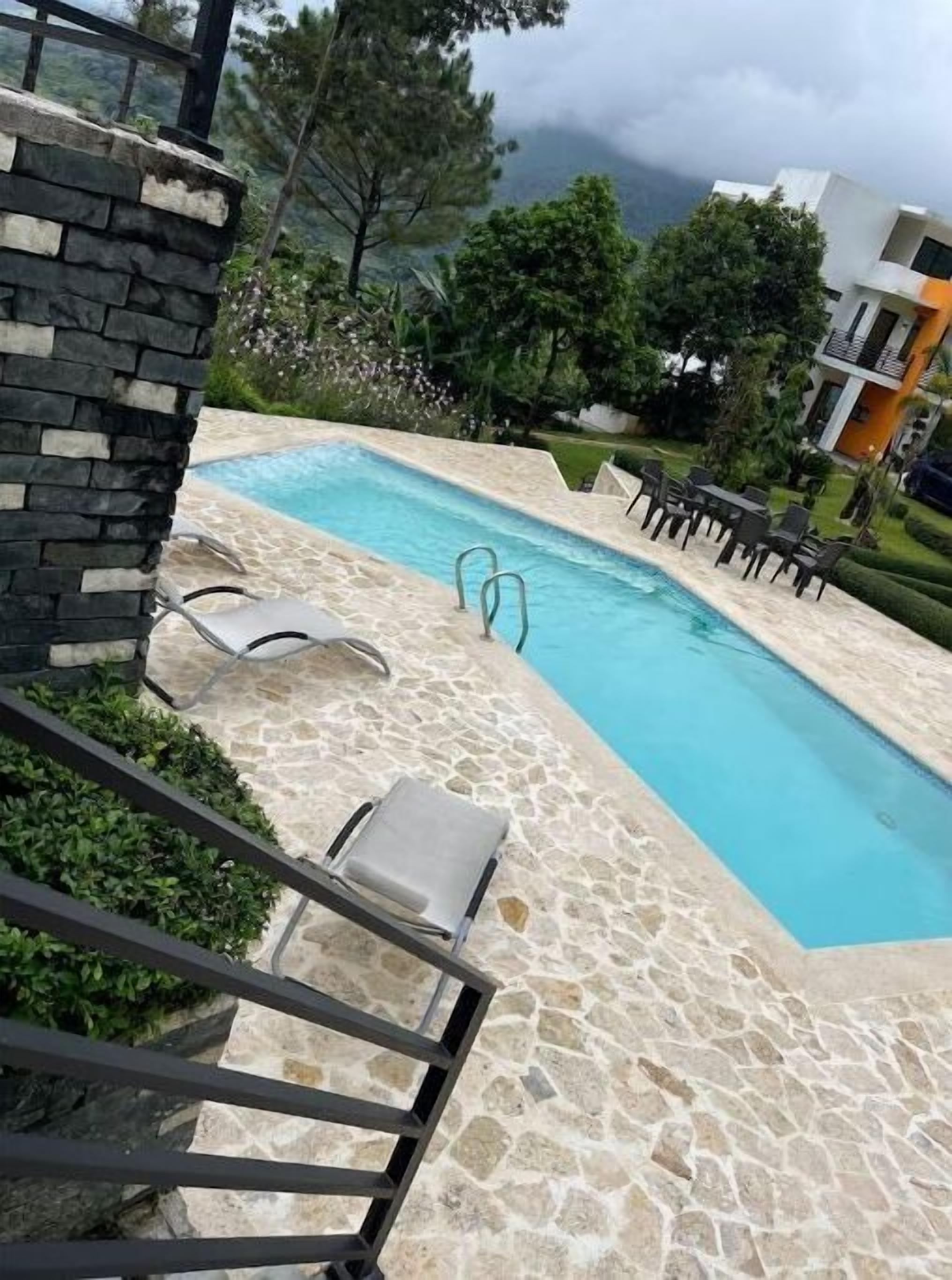 A swimming pool with stone tiles, lounge chairs, and a stone wall.