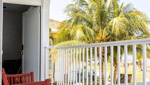 A balcony with a white railing, a wooden bench, and a view of palm trees.