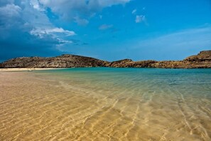 Una playa con aguas poco profundas y cristalinas, y colinas rocosas al fondo.