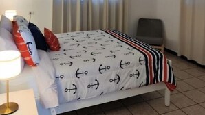 A hotel room with a bed, a chair, a lamp, and curtains.