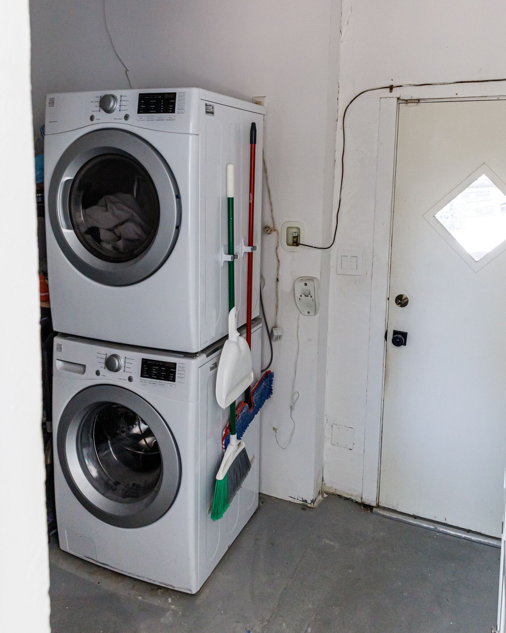 Un espace buanderie avec deux machines à laver superposées et un balai appuyé contre le mur.